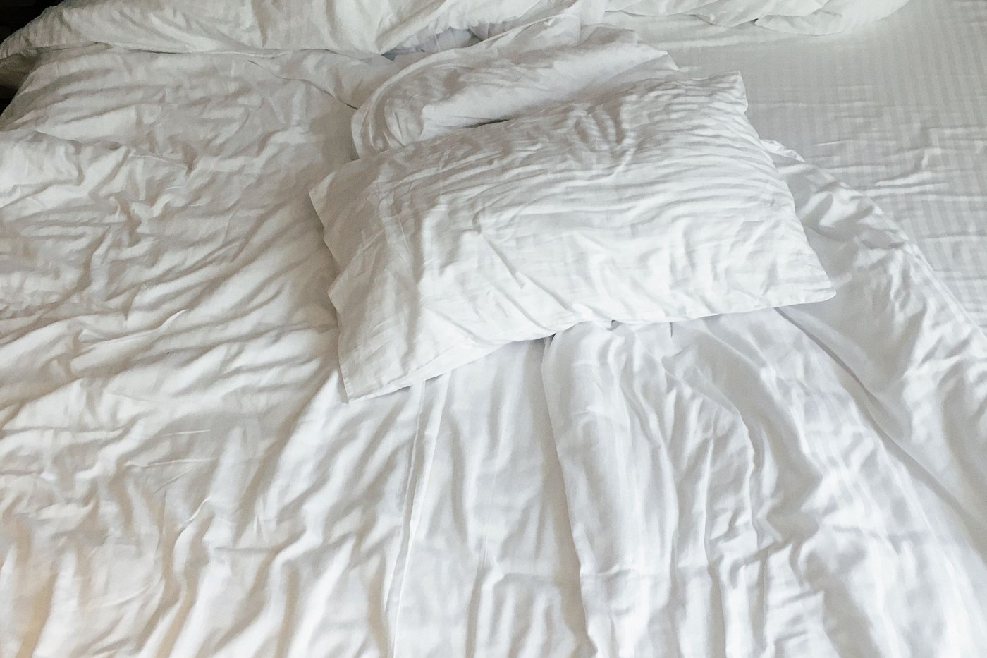 Cama de visitas feita com lençóis e almofadas brancas num quarto luminoso