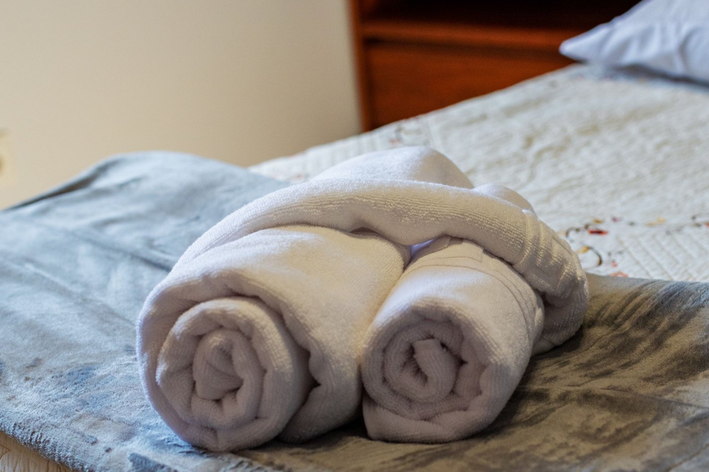 Toalhas enroladas pousadas sobre uma cama de hóspedes feita com roupa de cama branca